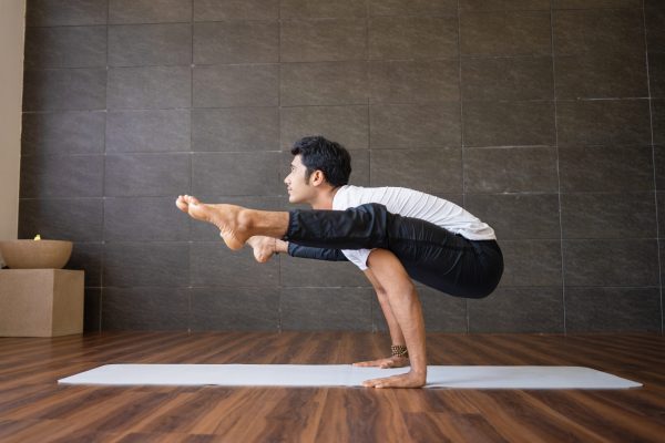 Indian yogi doing firefly yoga pose in gym. Man practicing advanced yoga. Yogi concept. Side view.